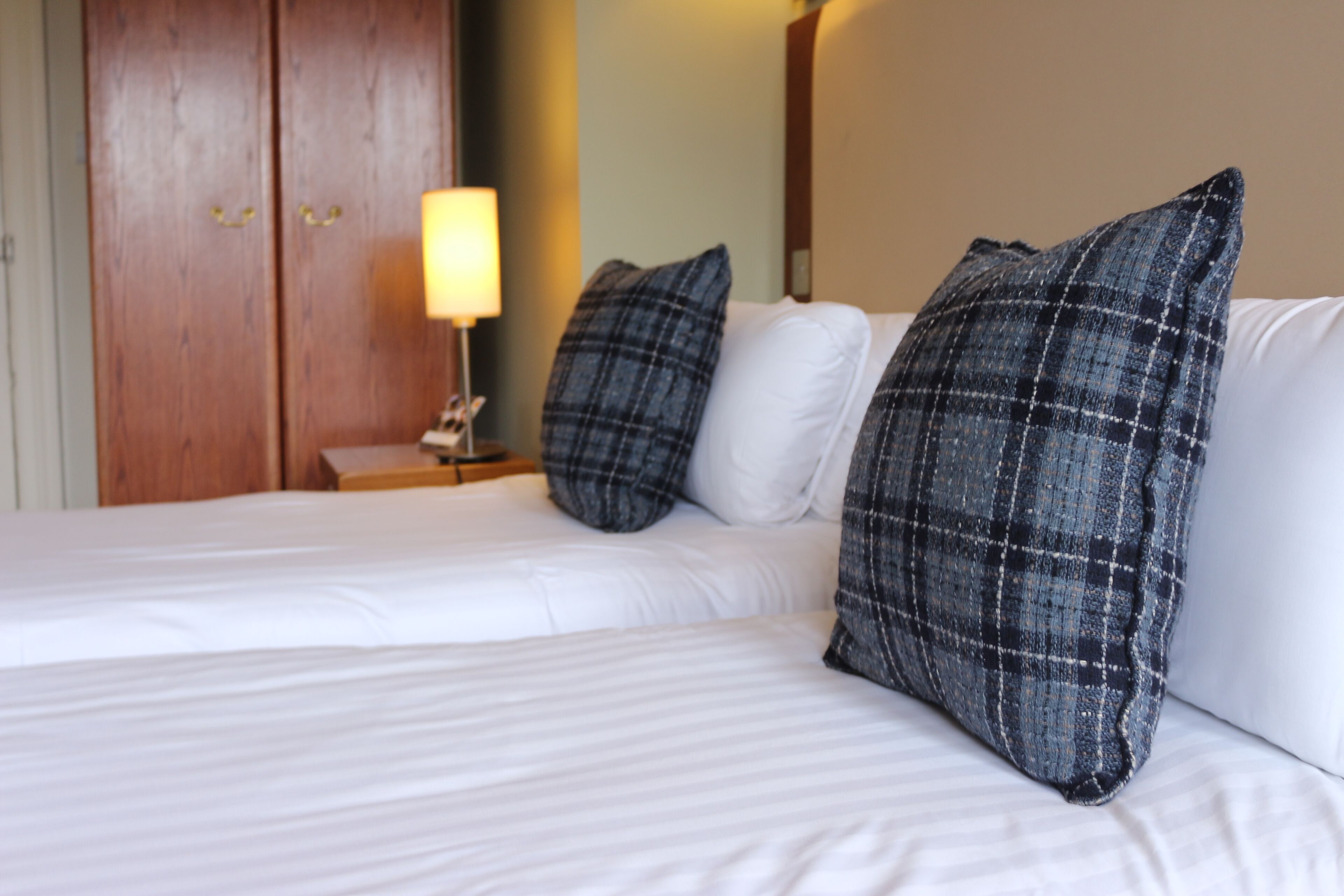 A hotel room with two beds, a wooden wardrobe, and a bedside lamp.