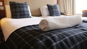 A hotel room with two beds, each with a white mattress and a dark checkered blanket. There are two dark checkered pillows on each bed. - Craiglynne Hotel (Grantown-on-Spey)