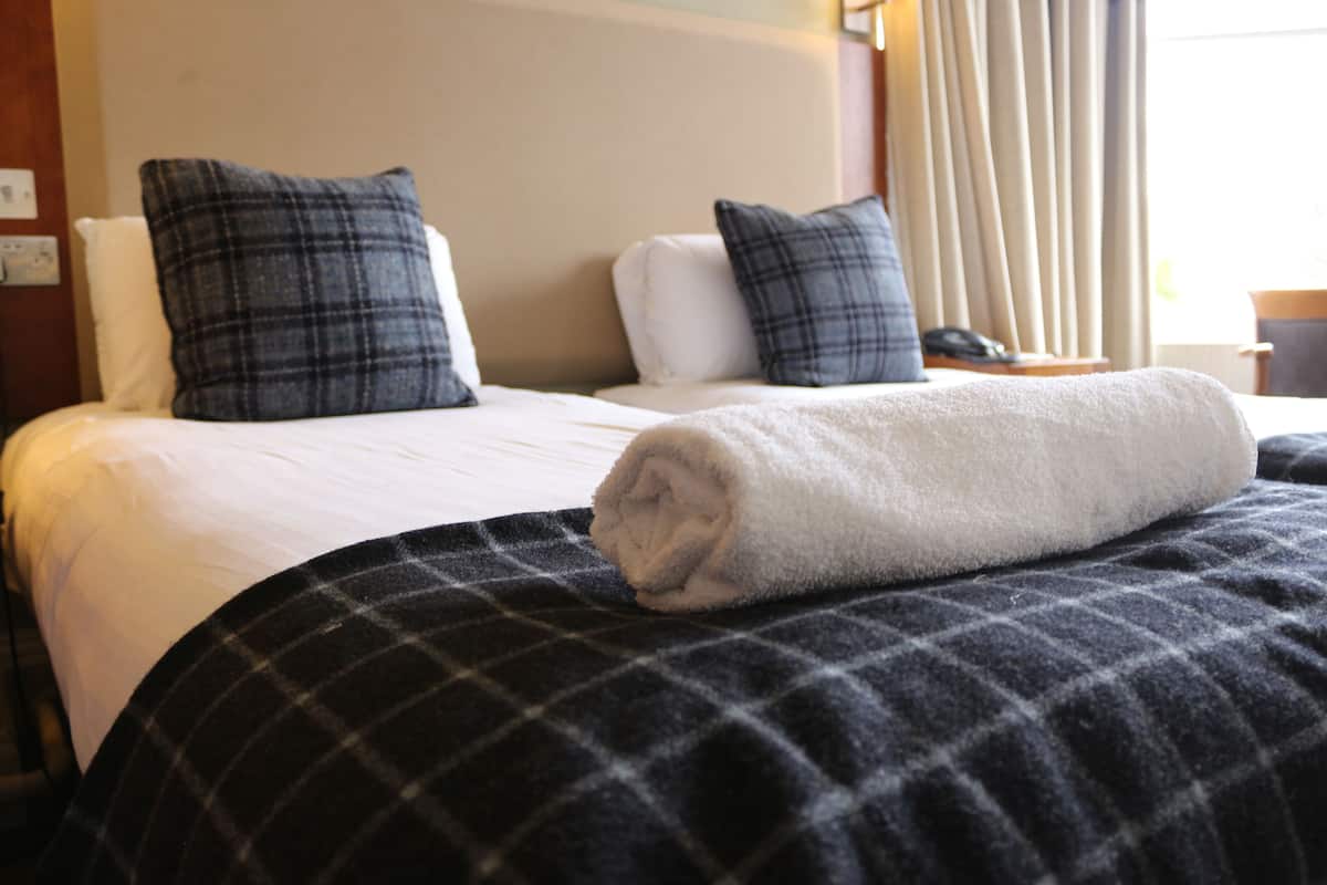 Une chambre d’hôtel avec deux lits, chacun doté d’un matelas blanc et d’une couverture à carreaux foncés. Chaque lit est agrémenté de deux oreillers à carreaux foncés.
