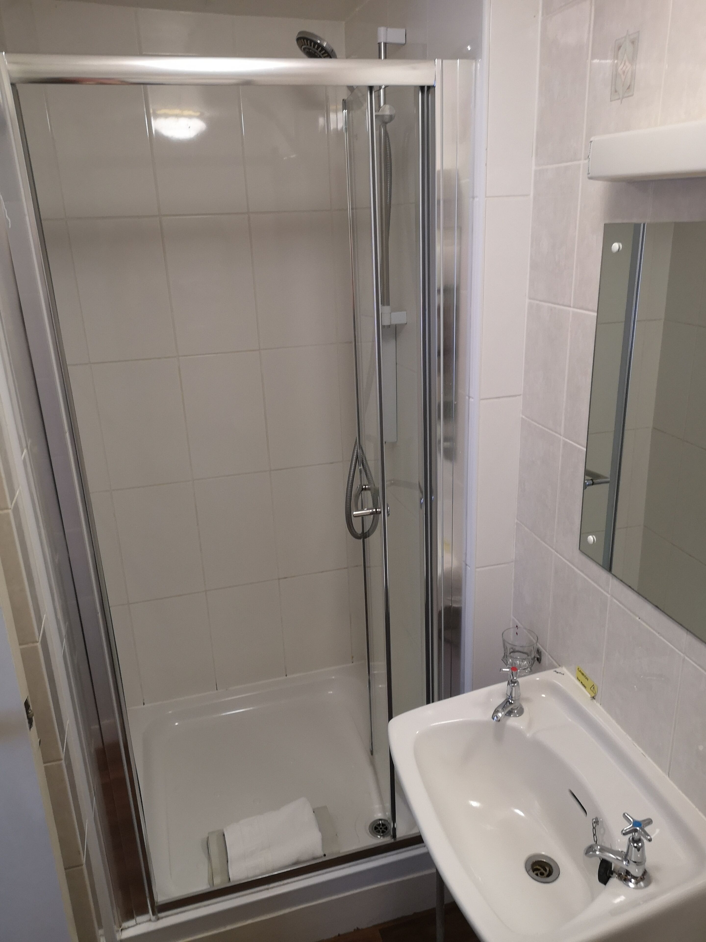 Un baño con ducha envuelta en vidrio, un lavabo blanco y un espejo sobre él.