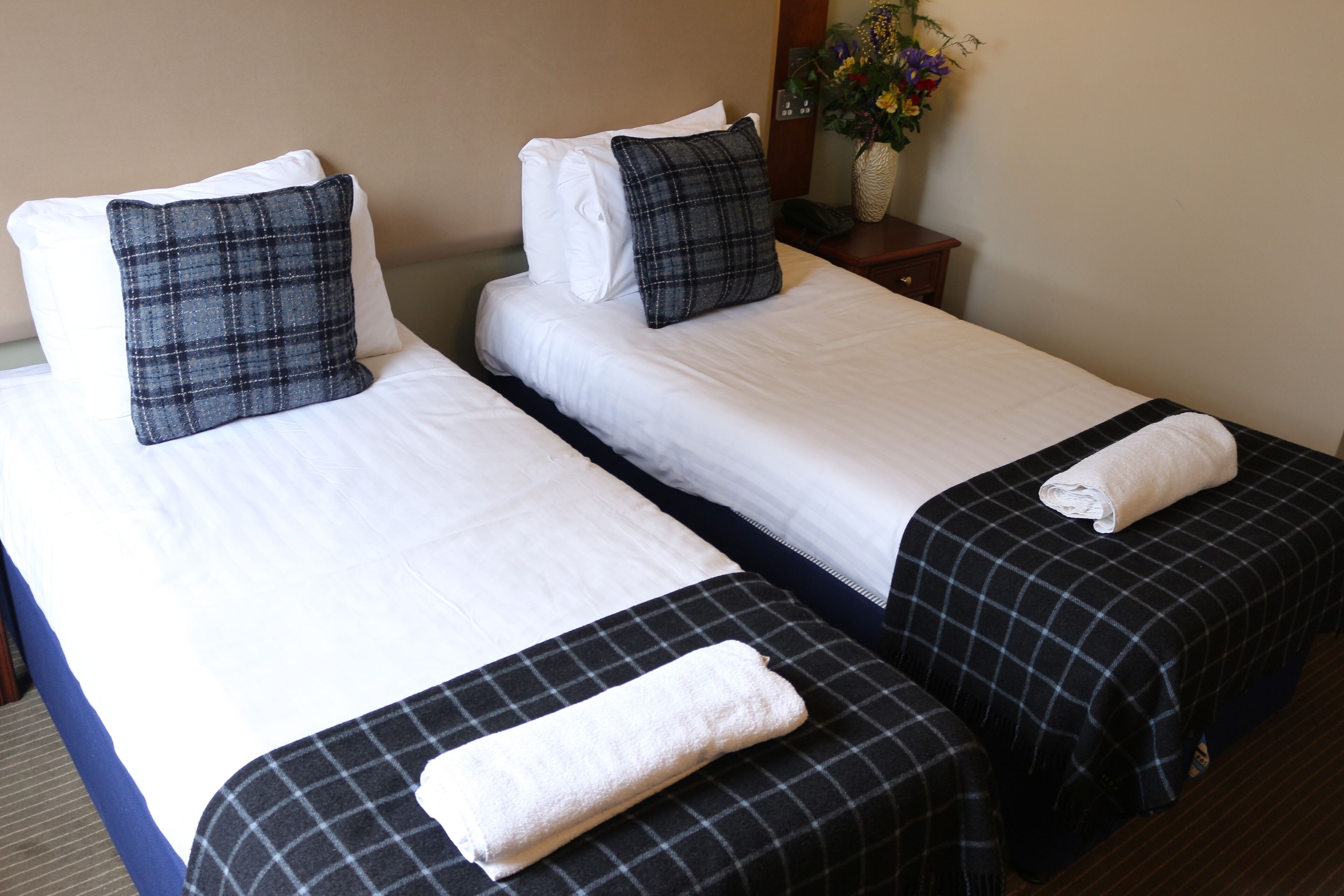 Two single beds with white and black checkered bedspreads, a white pillow, and a folded towel on each bed.