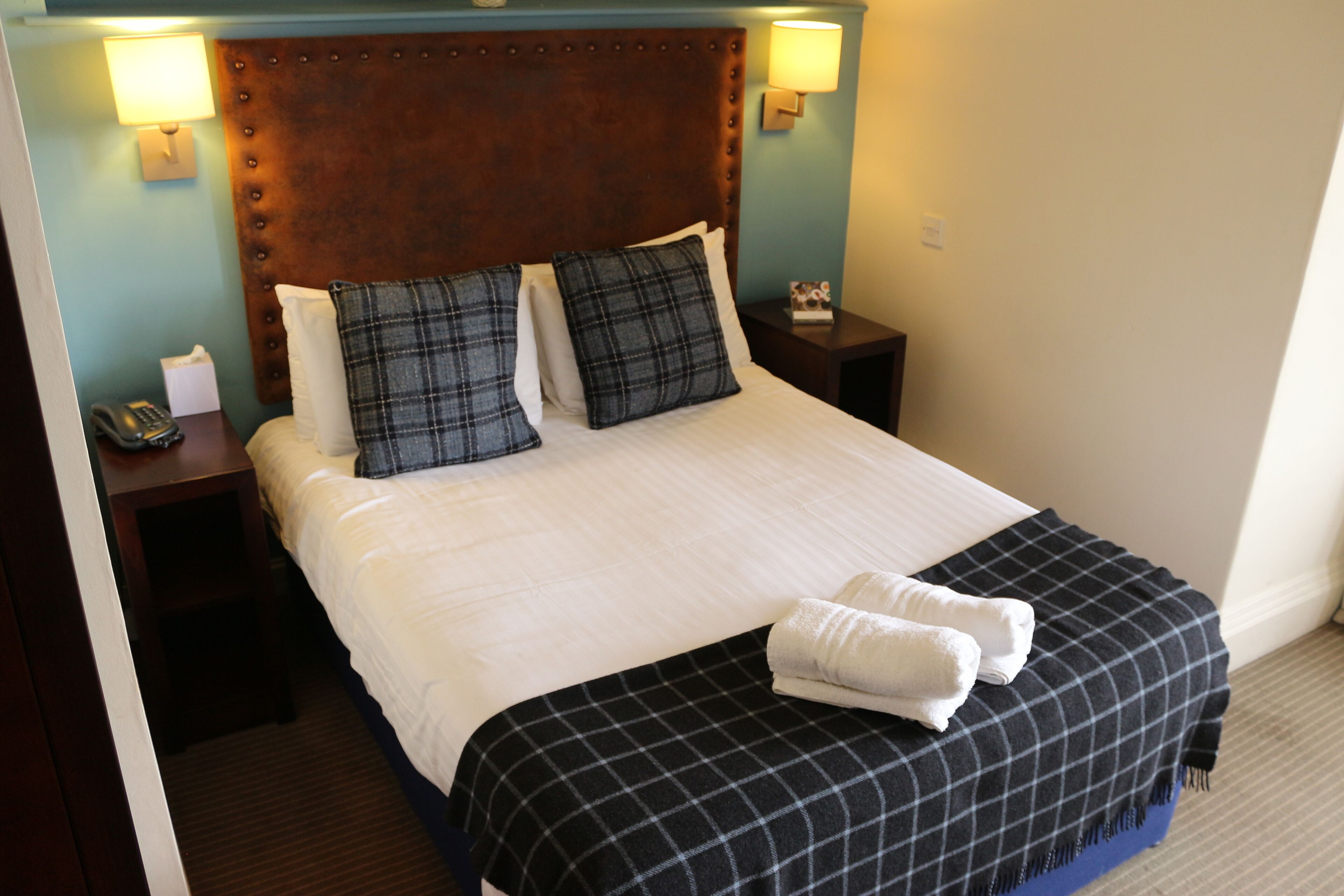 A hotel room with a large bed, two bedside tables, a telephone, and a lamp on each side.