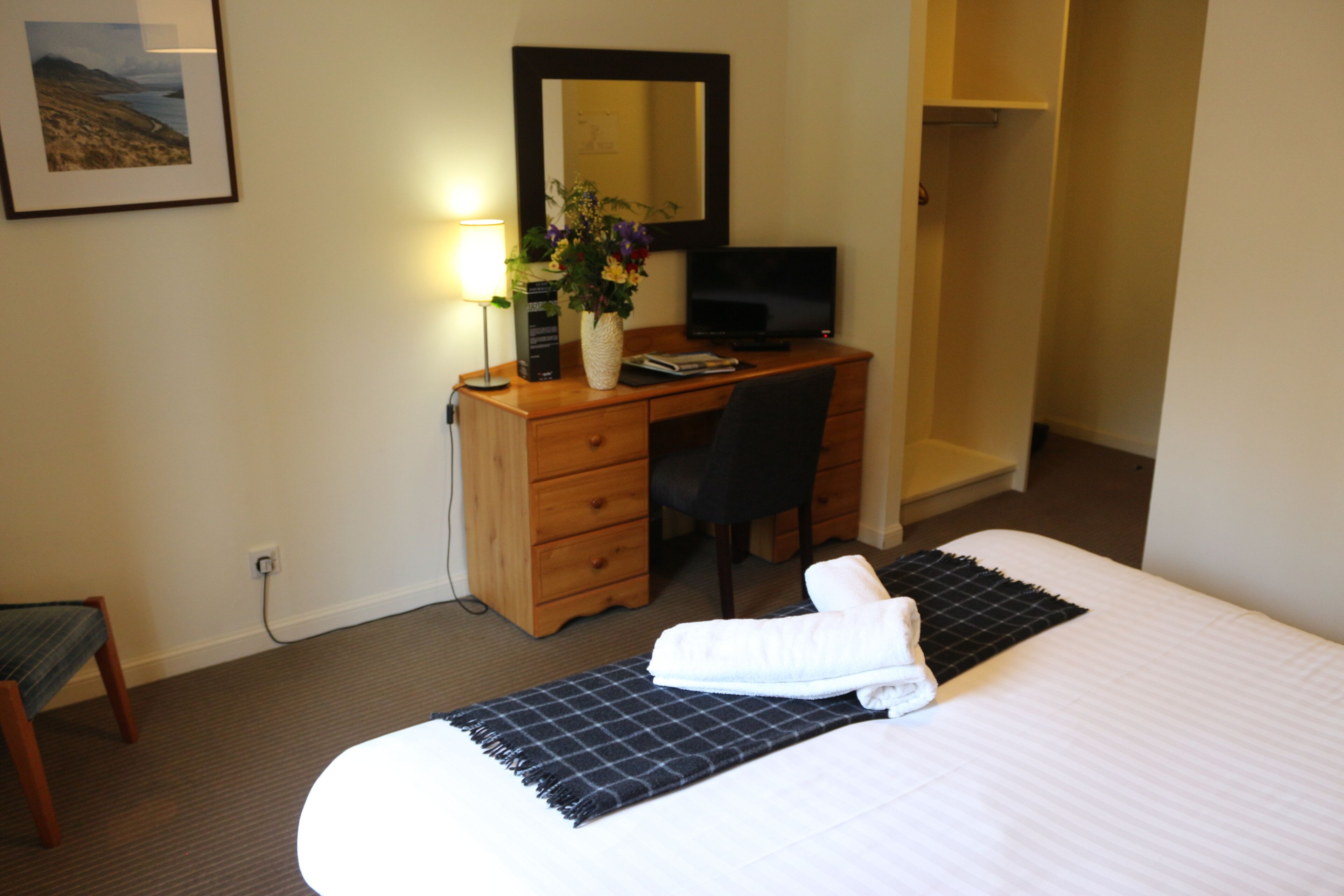 Una habitación de hotel con una cama, un escritorio con una computadora, una silla, una lámpara y un espejo.