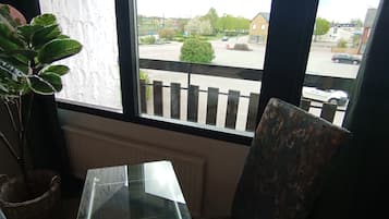 A room with a glass table and two patterned chairs, a potted plant, and a view of a street with cars and buildings.