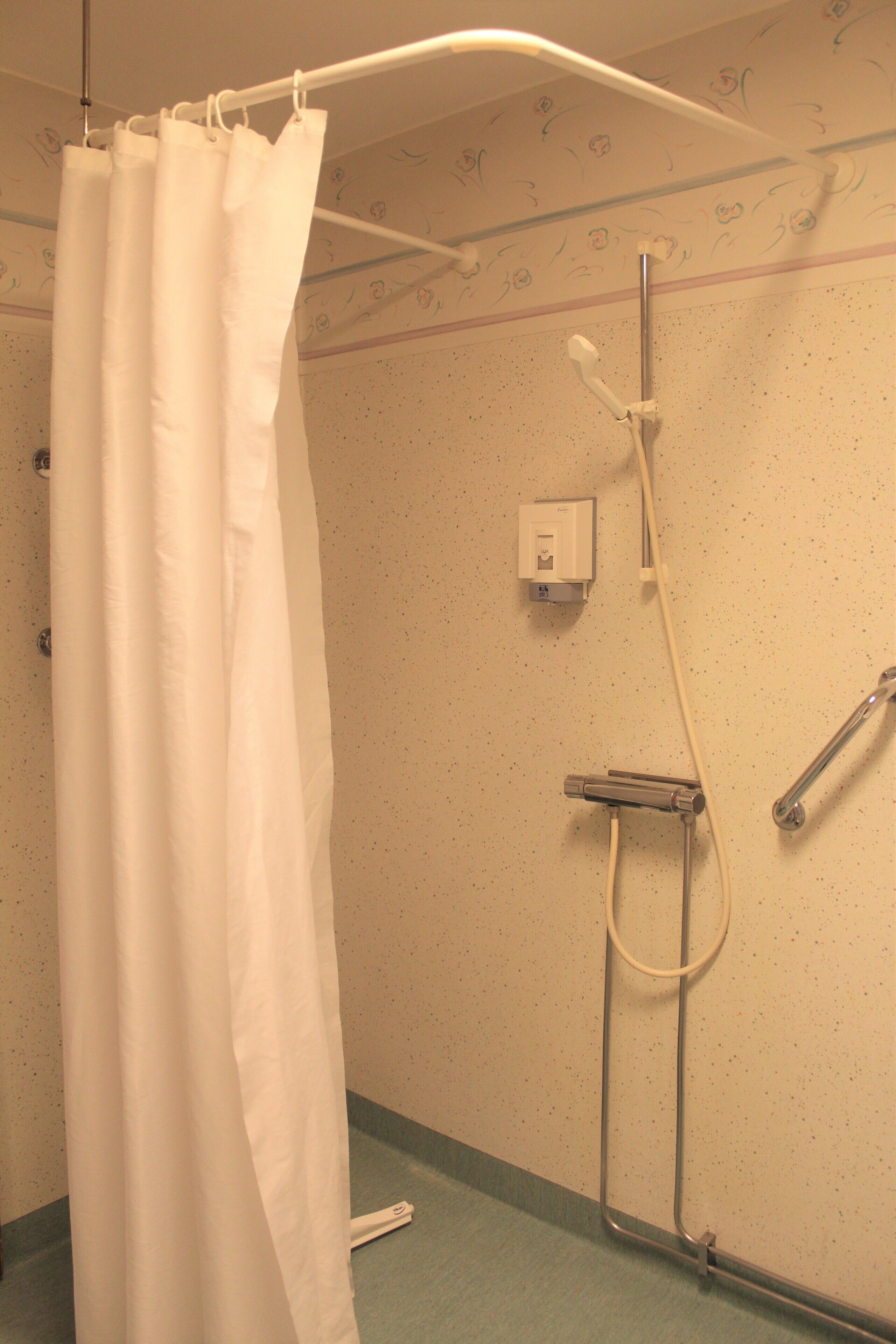 A shower area with a white shower curtain, a handheld showerhead, and a wall-mounted faucet.