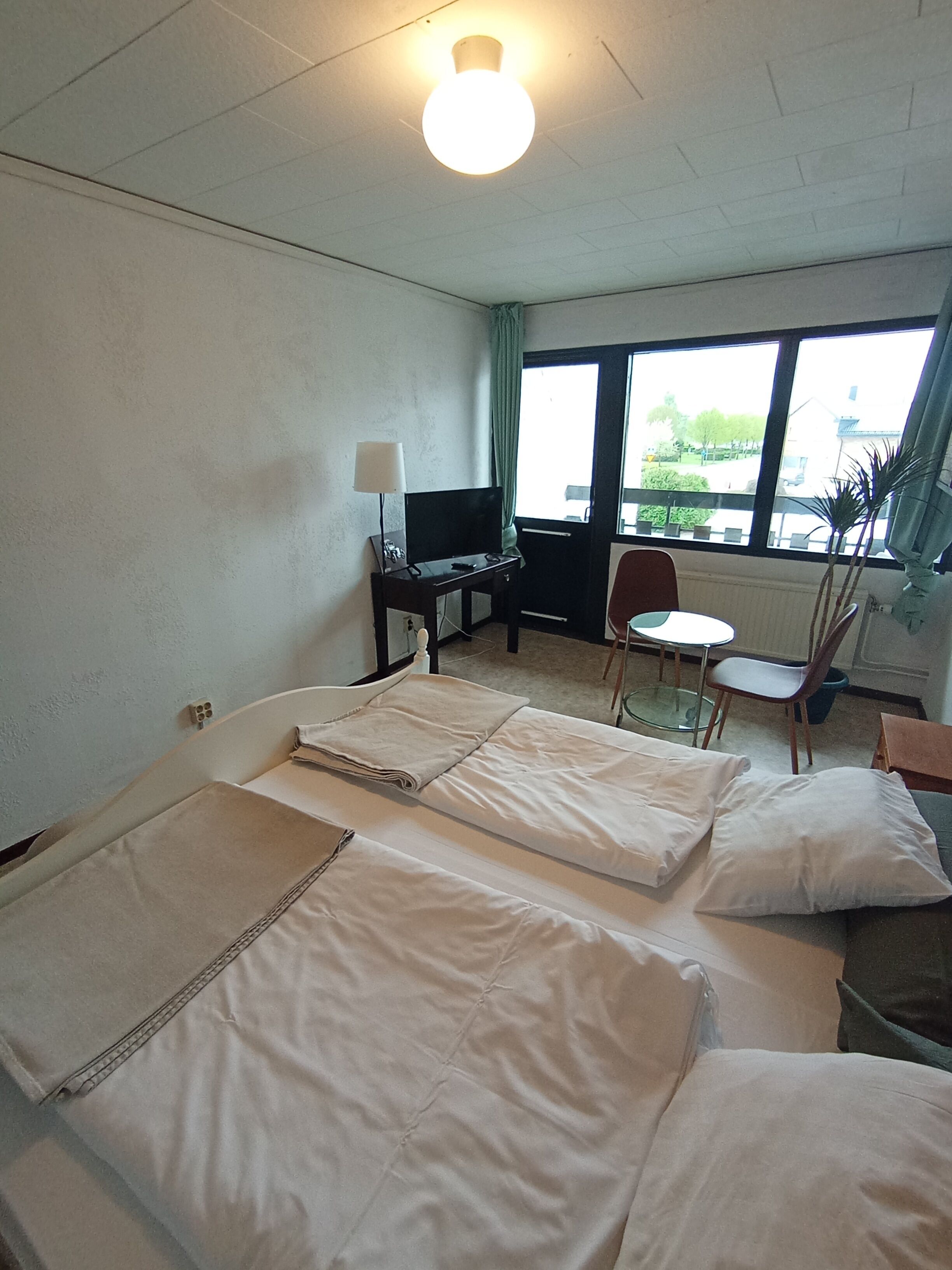 Ein Hotelzimmer mit zwei Betten, einem Schreibtisch mit Computer, einem Stuhl und einem Fenster mit Blick nach draußen.