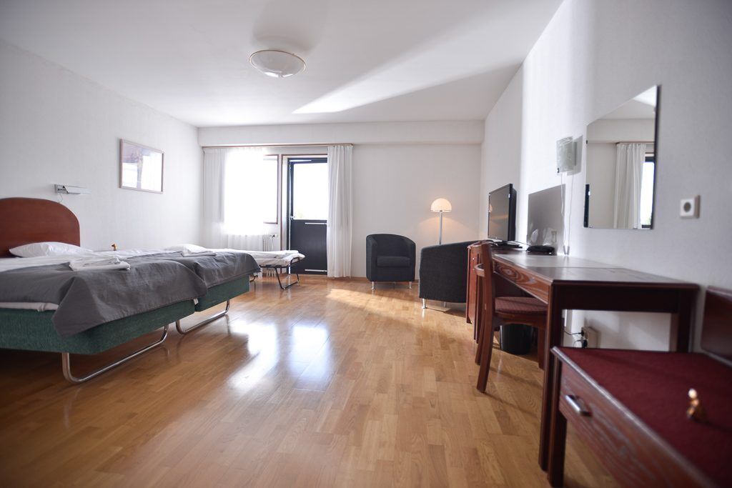 A hotel room with a bed, desk, chair, and a TV.