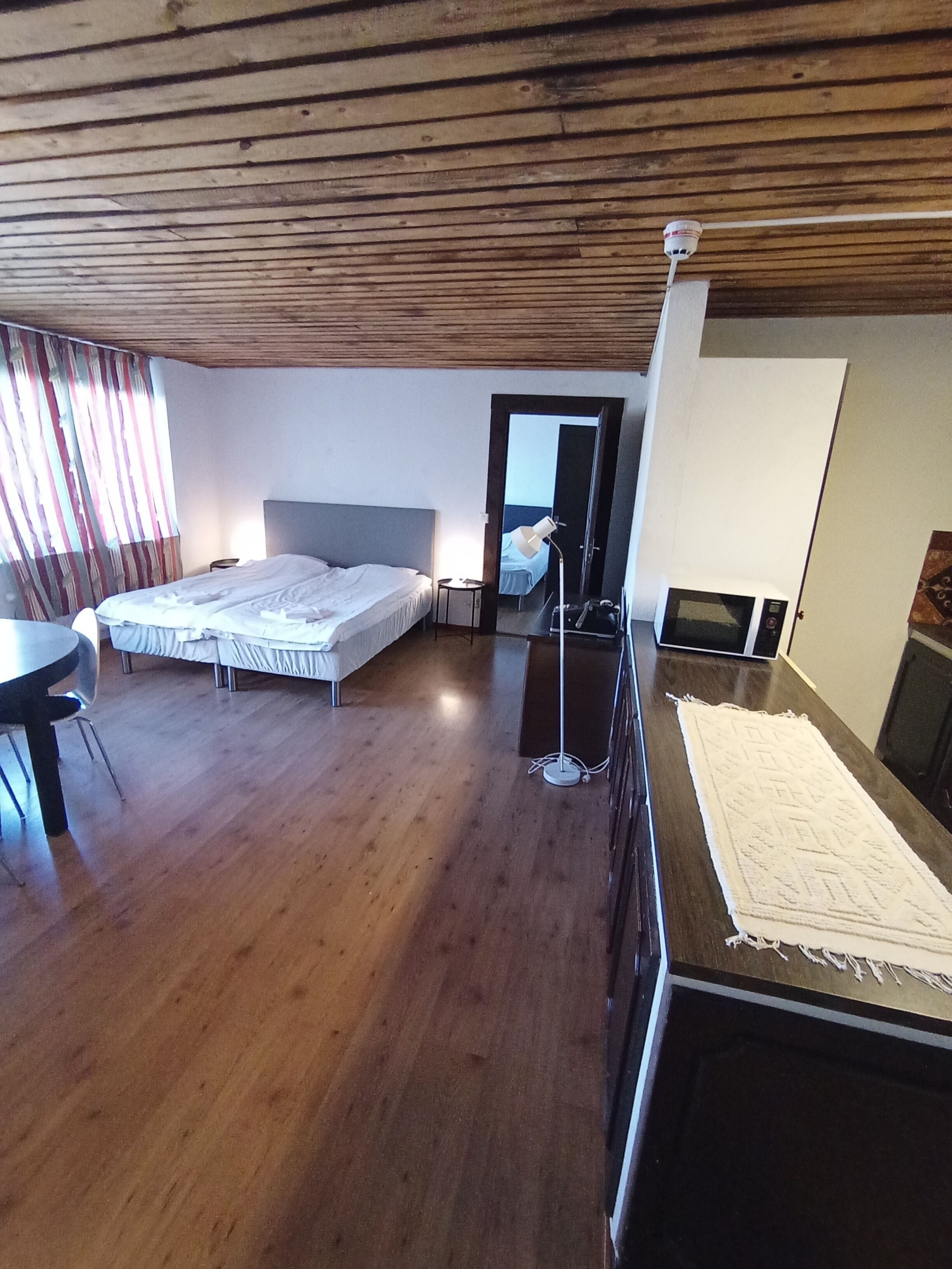 A room with wooden flooring, two beds, a desk, a chair, a lamp, and a microwave.