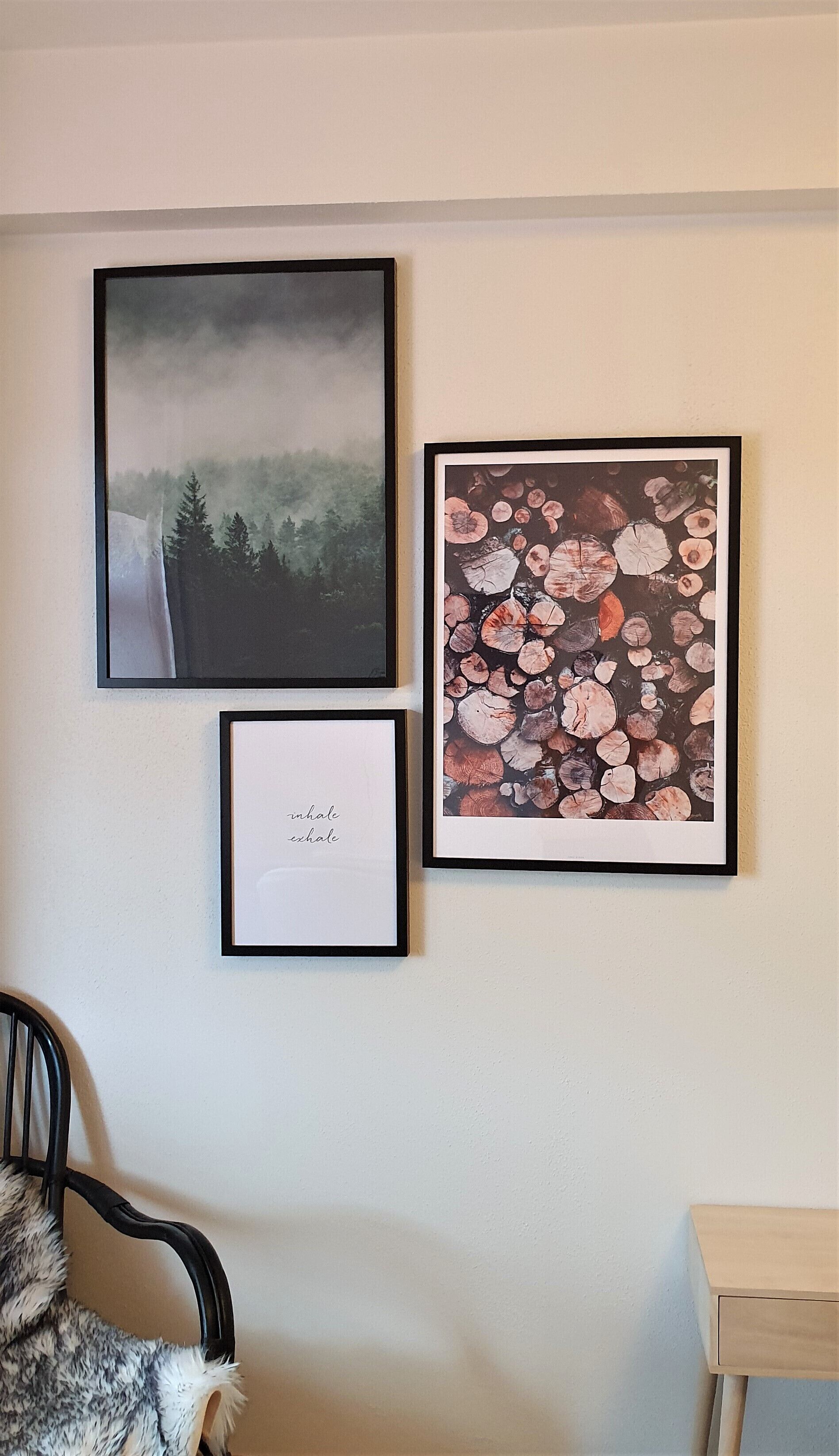 Three framed artworks on a wall, a chair, and a small table.