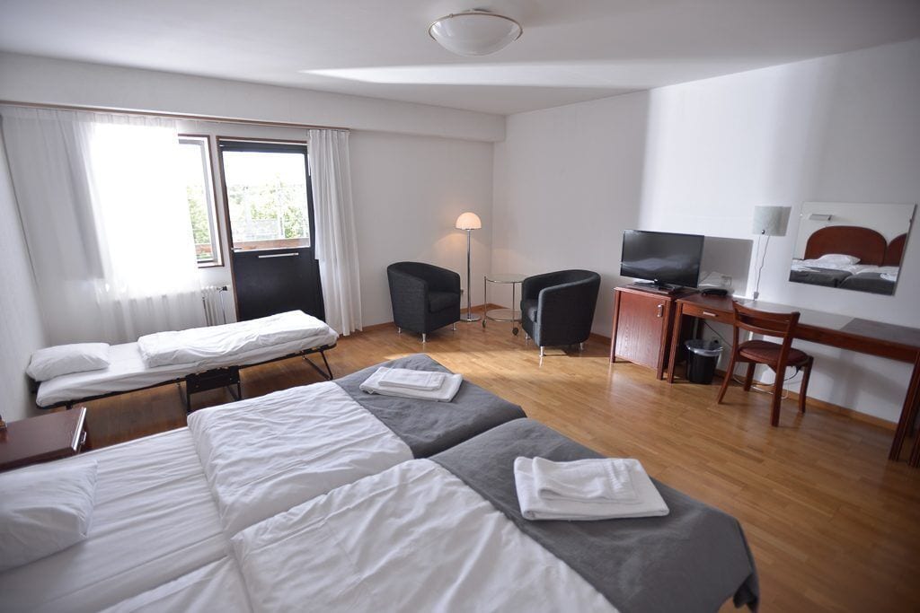 A hotel room with two beds, a desk, a chair, a television, and a lamp.