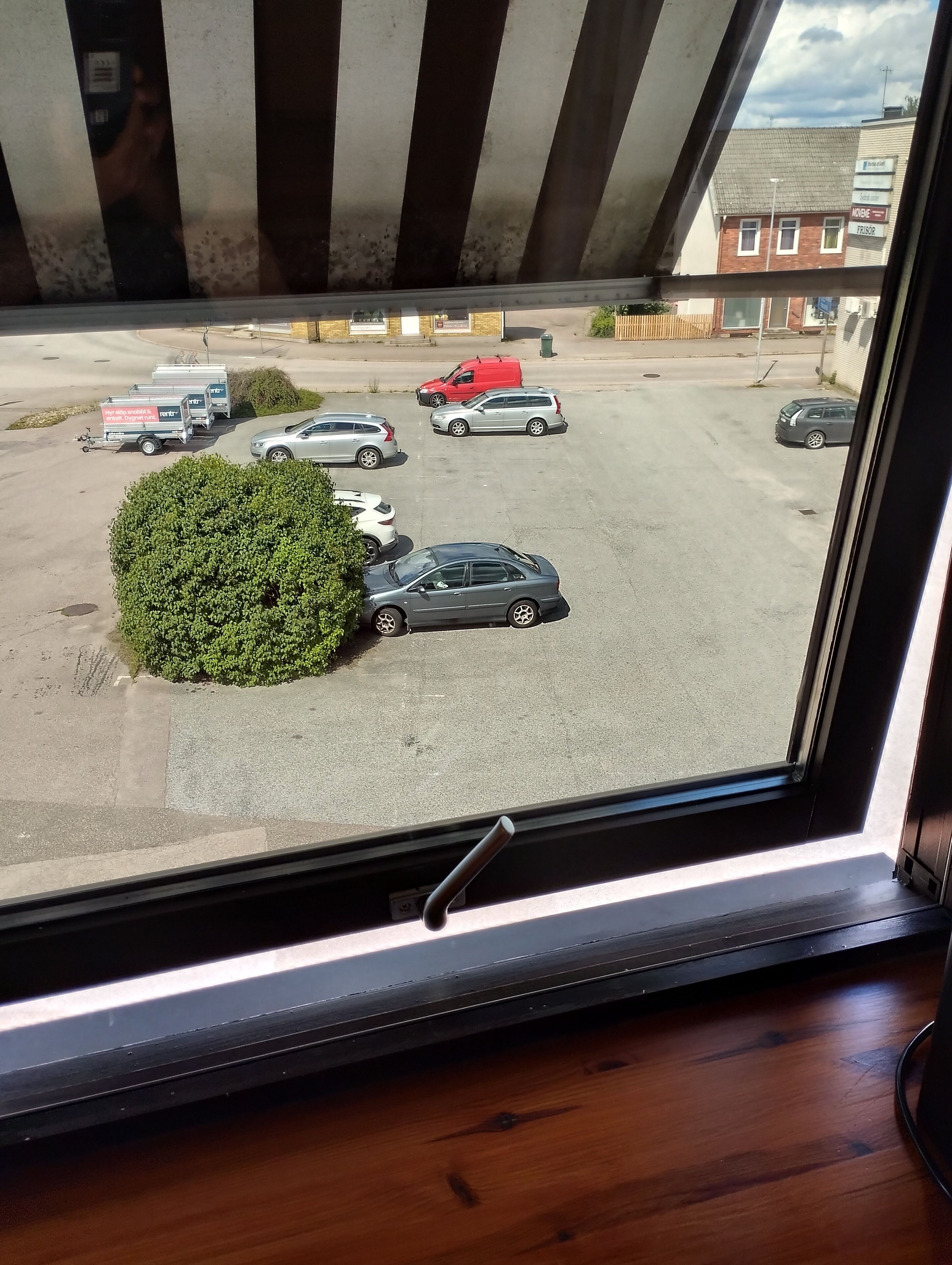 Un aparcamiento con varios coches y una furgoneta roja, visto a través de una ventana con suelo de madera.