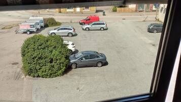 Un aparcamiento con varios coches y una furgoneta roja, visto a través de una ventana con suelo de madera.