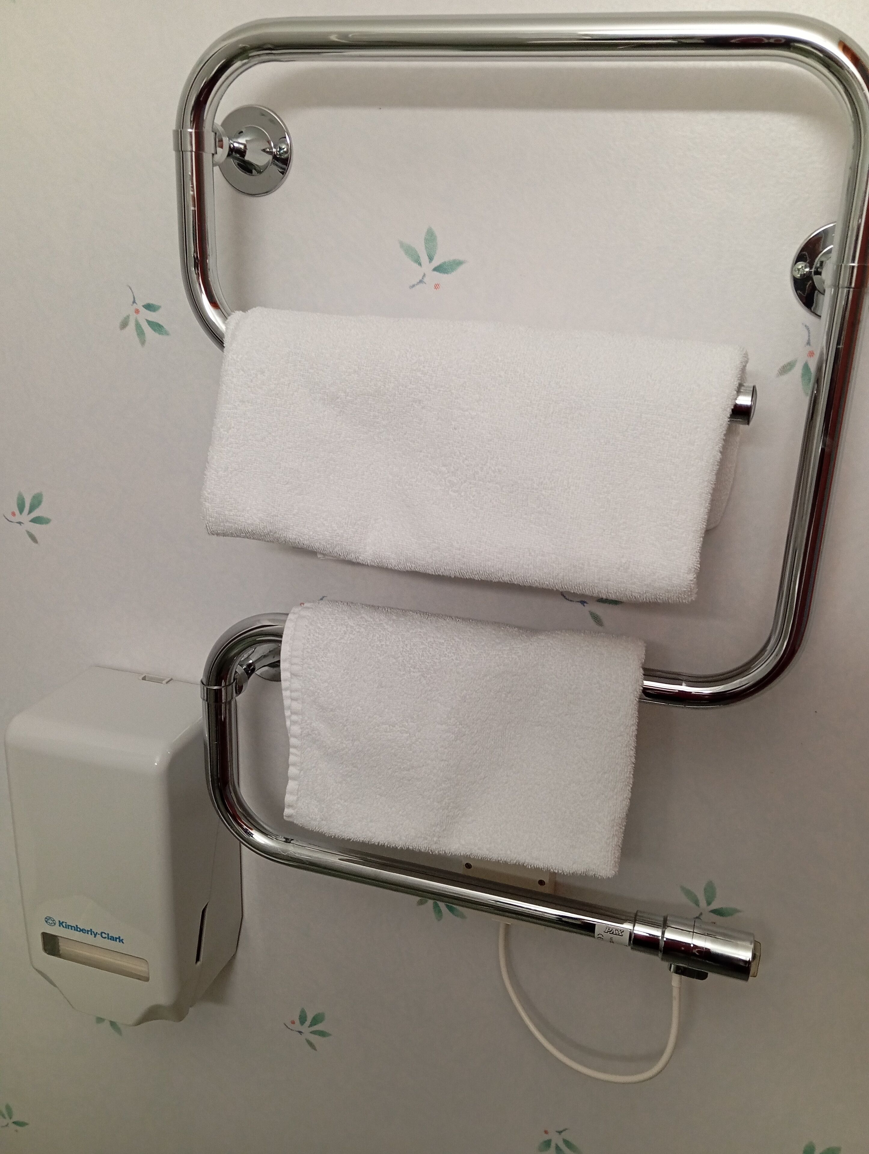A bathroom with a towel rack holding two white towels, a hand dryer, and a paper towel dispenser.
