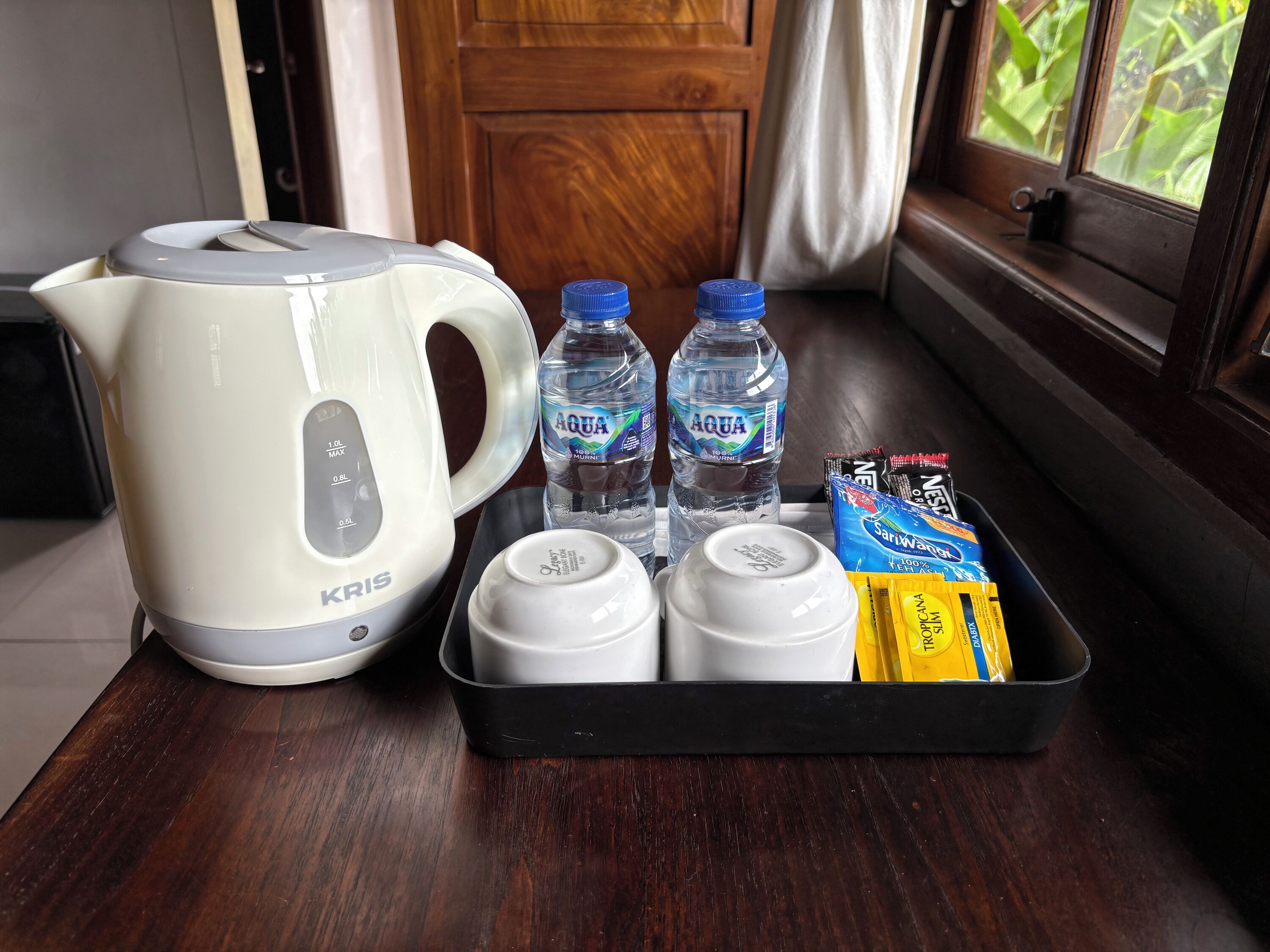 Una cocina con un hervidor eléctrico blanco, dos botellas de agua, y una bandeja con tazas y bolsitas de té.