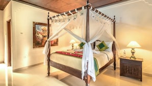 A four-poster bed with a canopy, a bedside table with a lamp, and a painting on the wall. - Hotel Bunga Permai (Ubud)