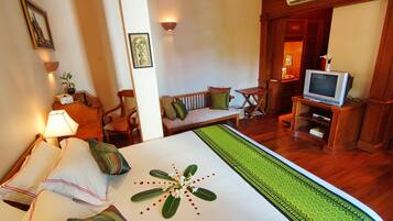 Habitación de hotel con cama, televisor sobre un mueble bajo, sofá, sillón y una mesita.