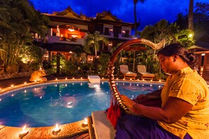 Relax by the serene pool surrounded by lush gardens and a traditional building with a tiled roof.