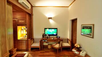 Una habitación con un escritorio de madera, dos sillas, un televisor y una pequeña mesa con fruta.