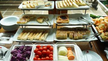 A buffet with various food items including bread, pastries, and fresh vegetables.
