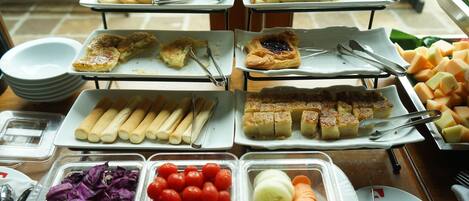 A buffet with various food items including bread, pastries, and fresh vegetables.