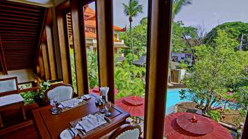 A dining area with a table set for two, overlooking a pool and lush greenery.