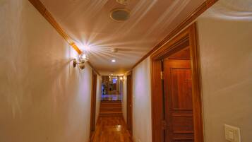 A hallway with wooden floors, a wooden door on the right, and a light fixture on the left.