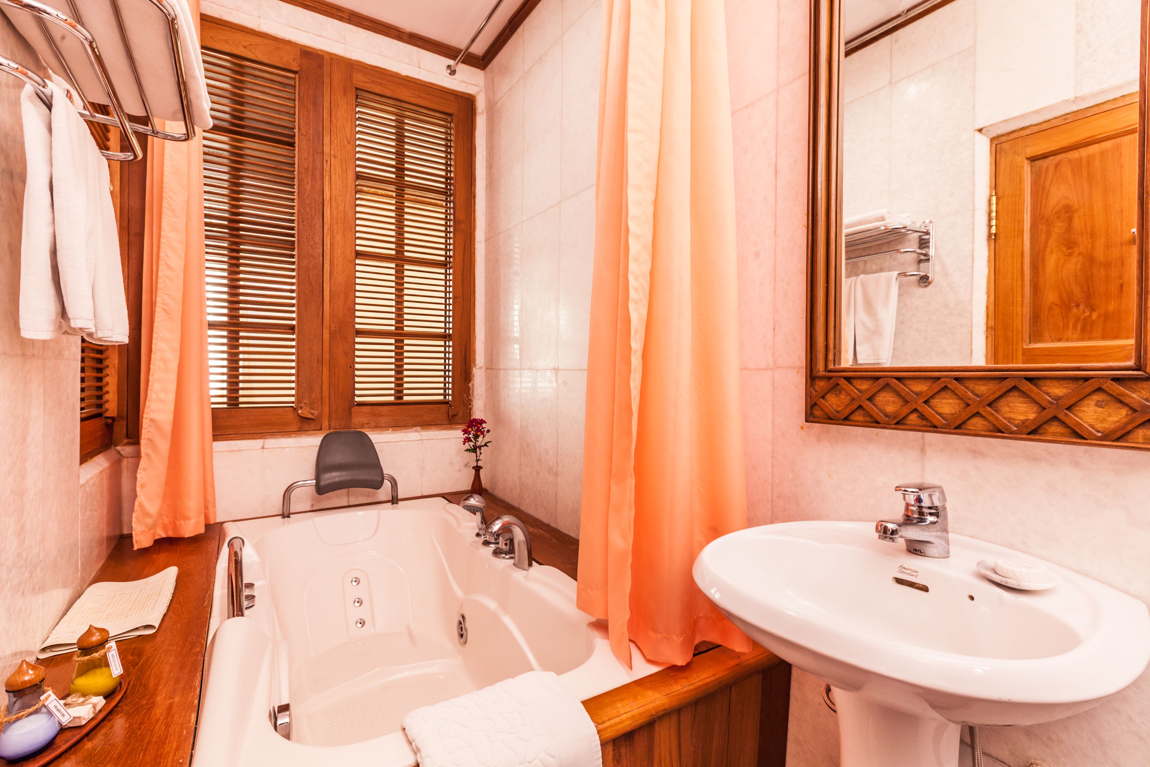 A bathroom with a bathtub, a sink, wooden blinds, and a mirror.
