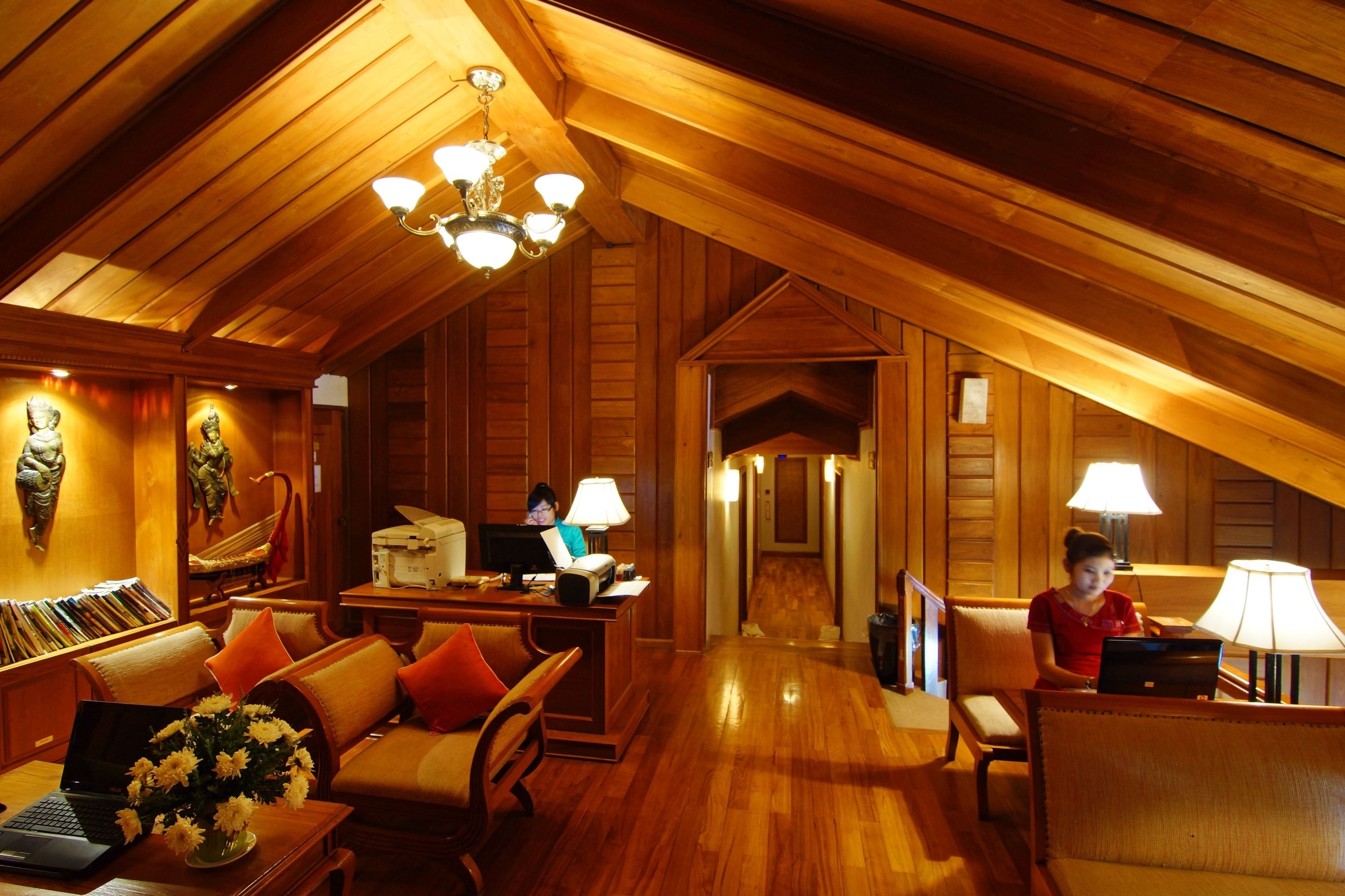 A wooden interior with a reception desk, seating area, and a hallway leading to another room.