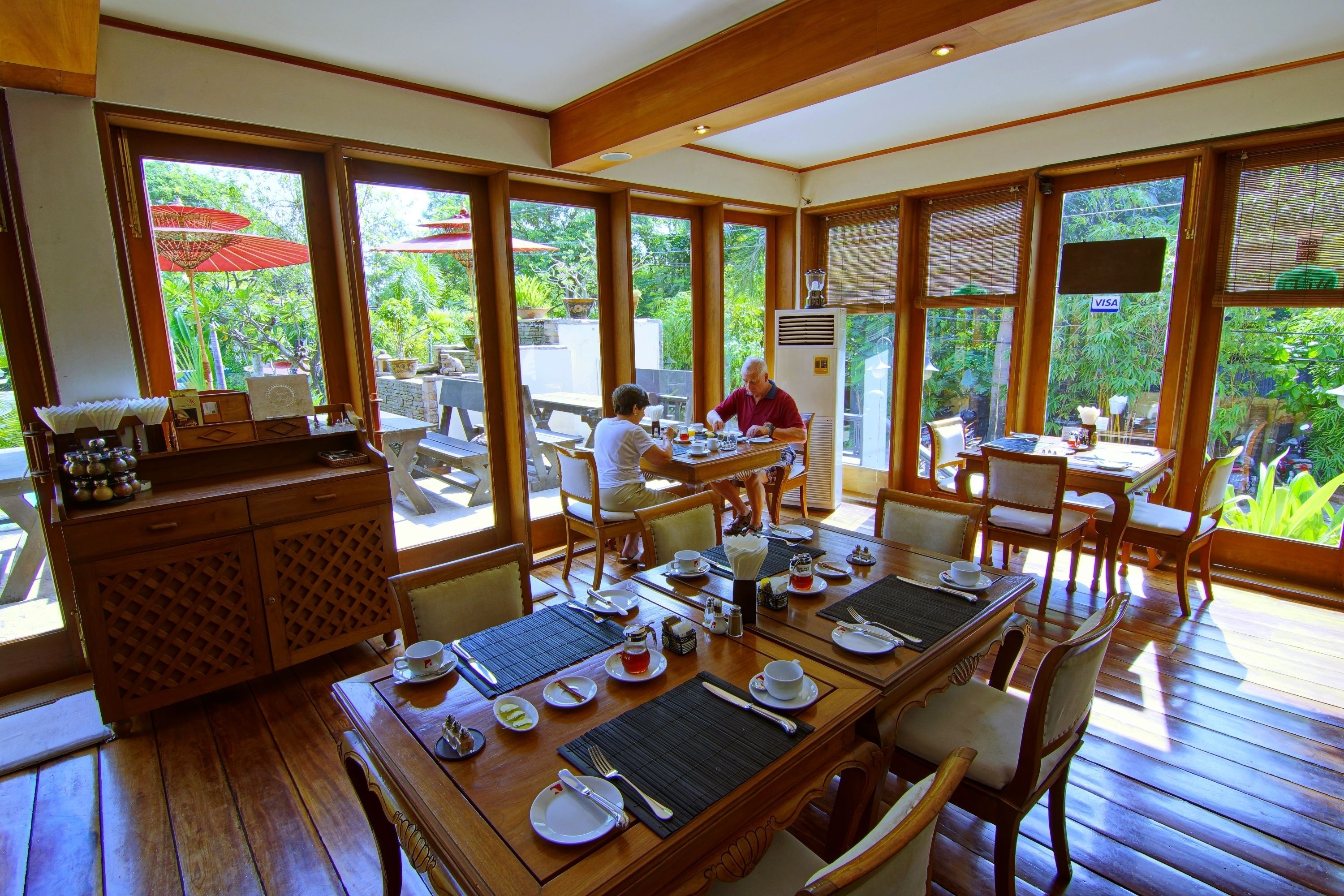 A dining area with wooden tables and chairs, a buffet counter, and large windows offering a view of the outdoors.