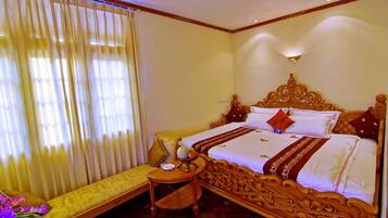 A hotel room with a large bed, a bedside table, a small table with a vase of flowers, and a bench with cushions.