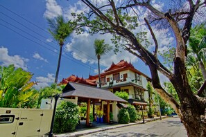 A traditional building with a red roof, surrounded by lush greenery and palm trees. - Hotel by the Red Canal (Mandalay)