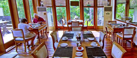 Un comedor con mesas dispuestas para comer, ventanas amplias y vistas a zonas verdes.