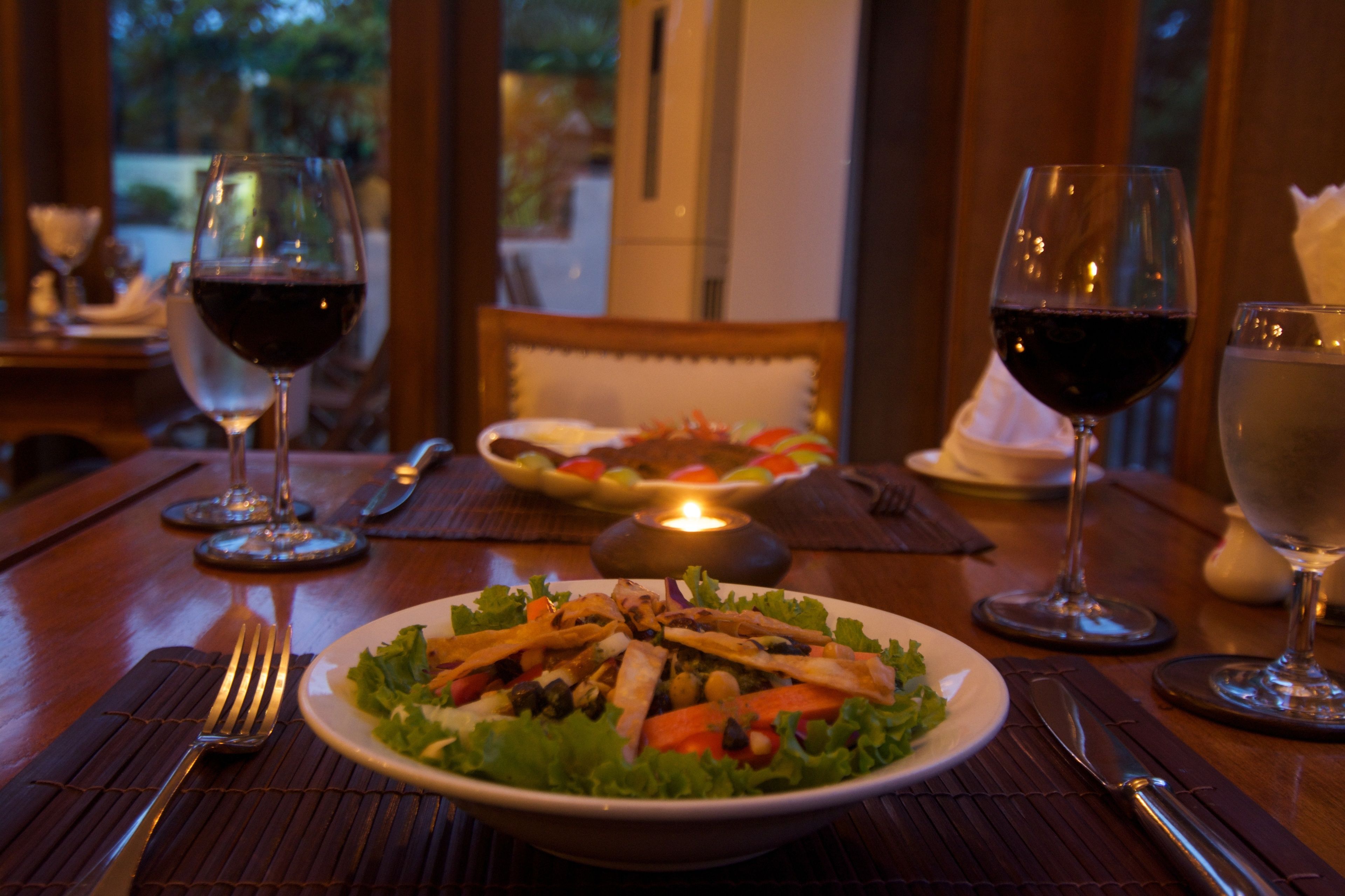 Una mesa de comedor con una ensalada en un plato, dos copas de vino y cubiertos.