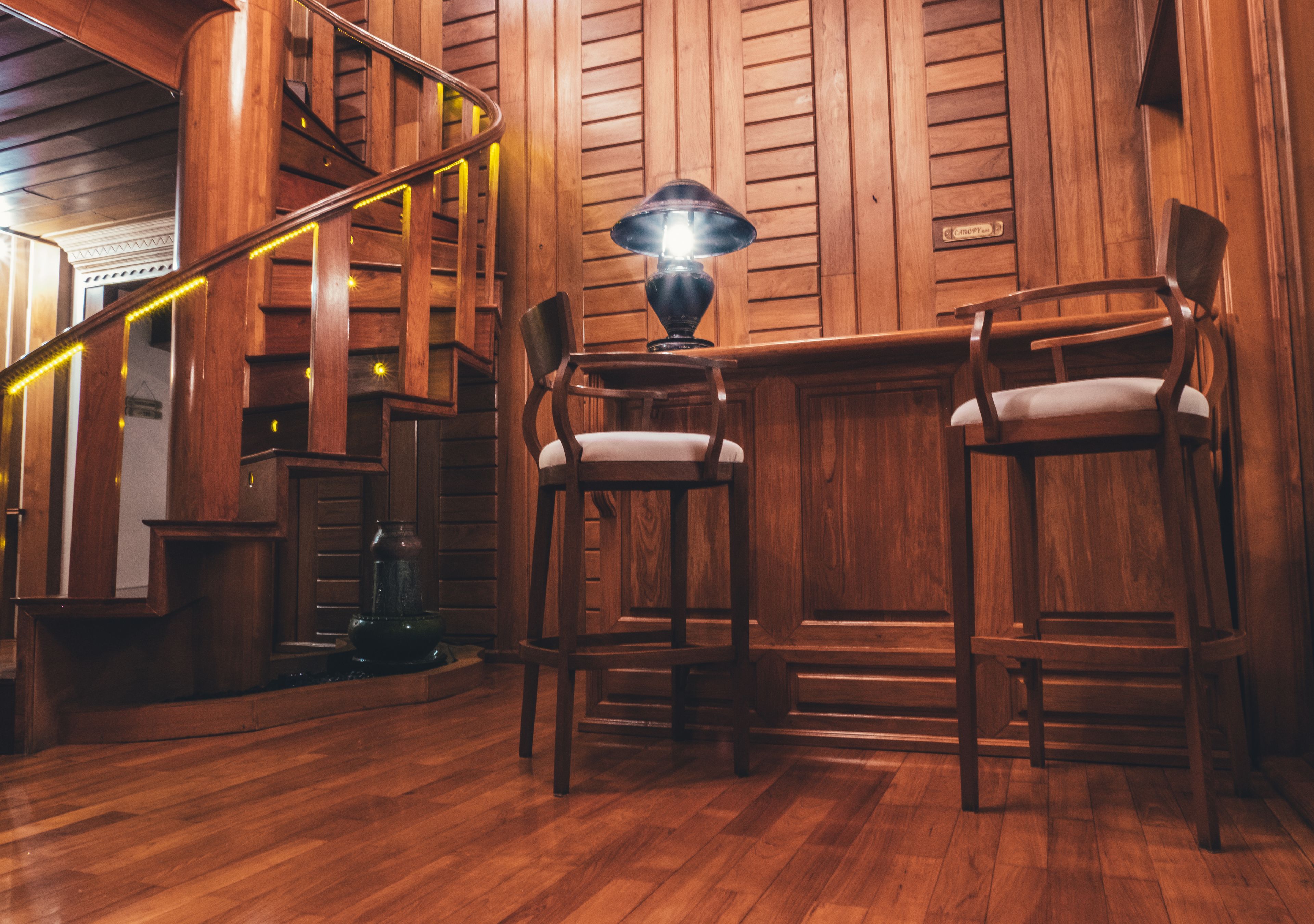 A wooden staircase with a railing, two bar stools, and a table lamp.