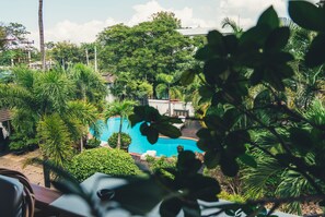 A view of a swimming pool surrounded by lush greenery and a building in the background. - Hotel by the Red Canal (Mandalay)