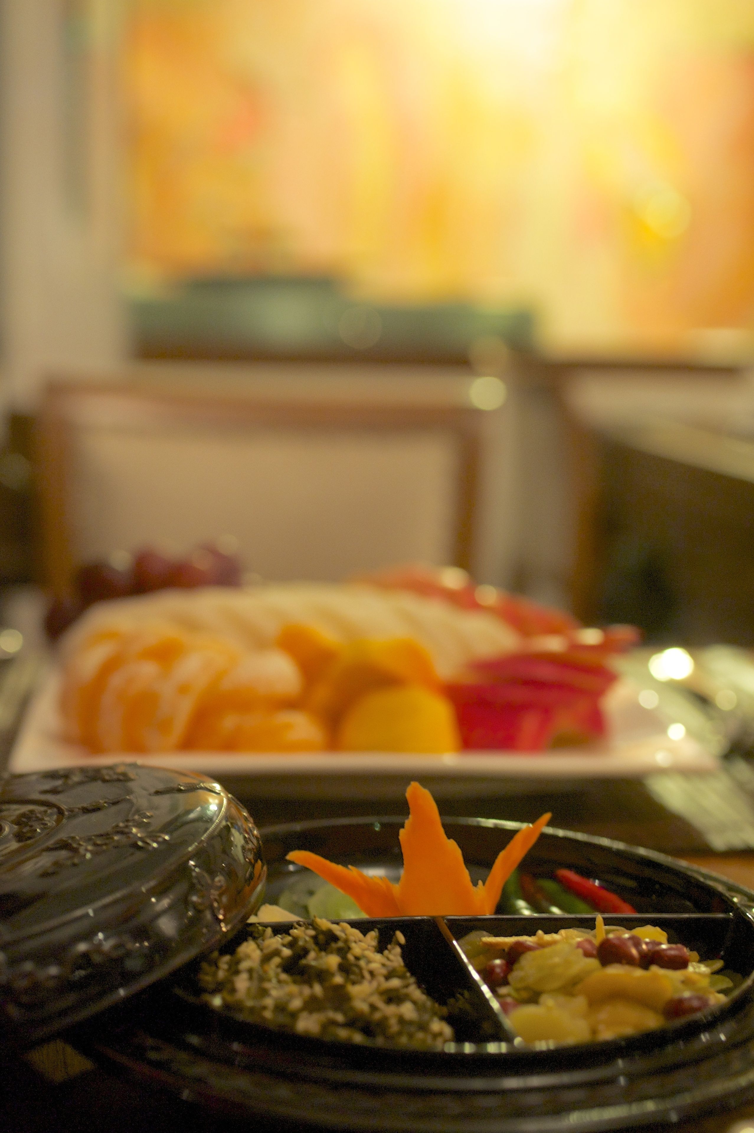 Una mesa de comedor con diversos platos, incluyendo un plato con frutas y verduras cortadas, un tazón de arroz y un adorno.