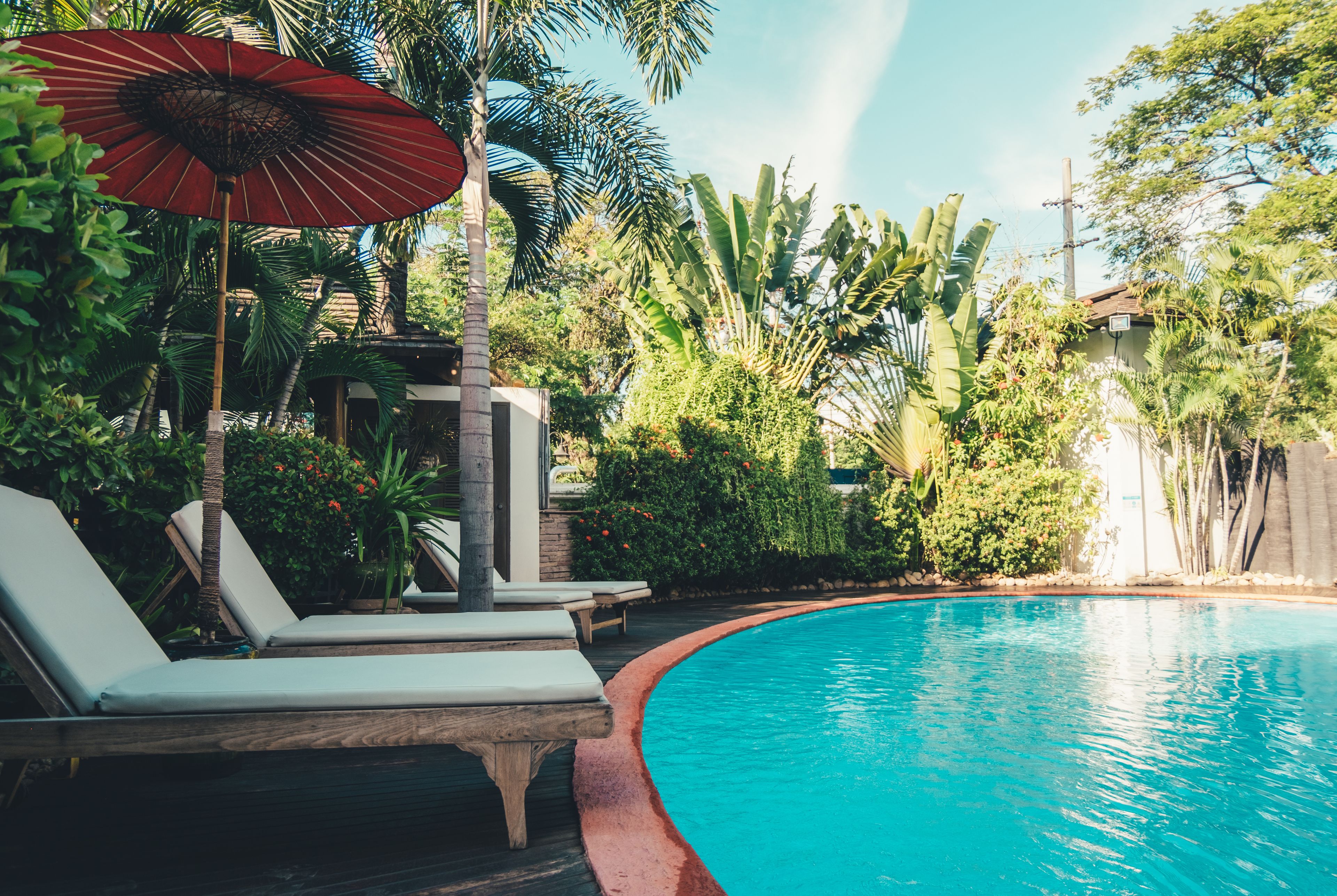 A poolside area with lounge chairs and a red umbrella.