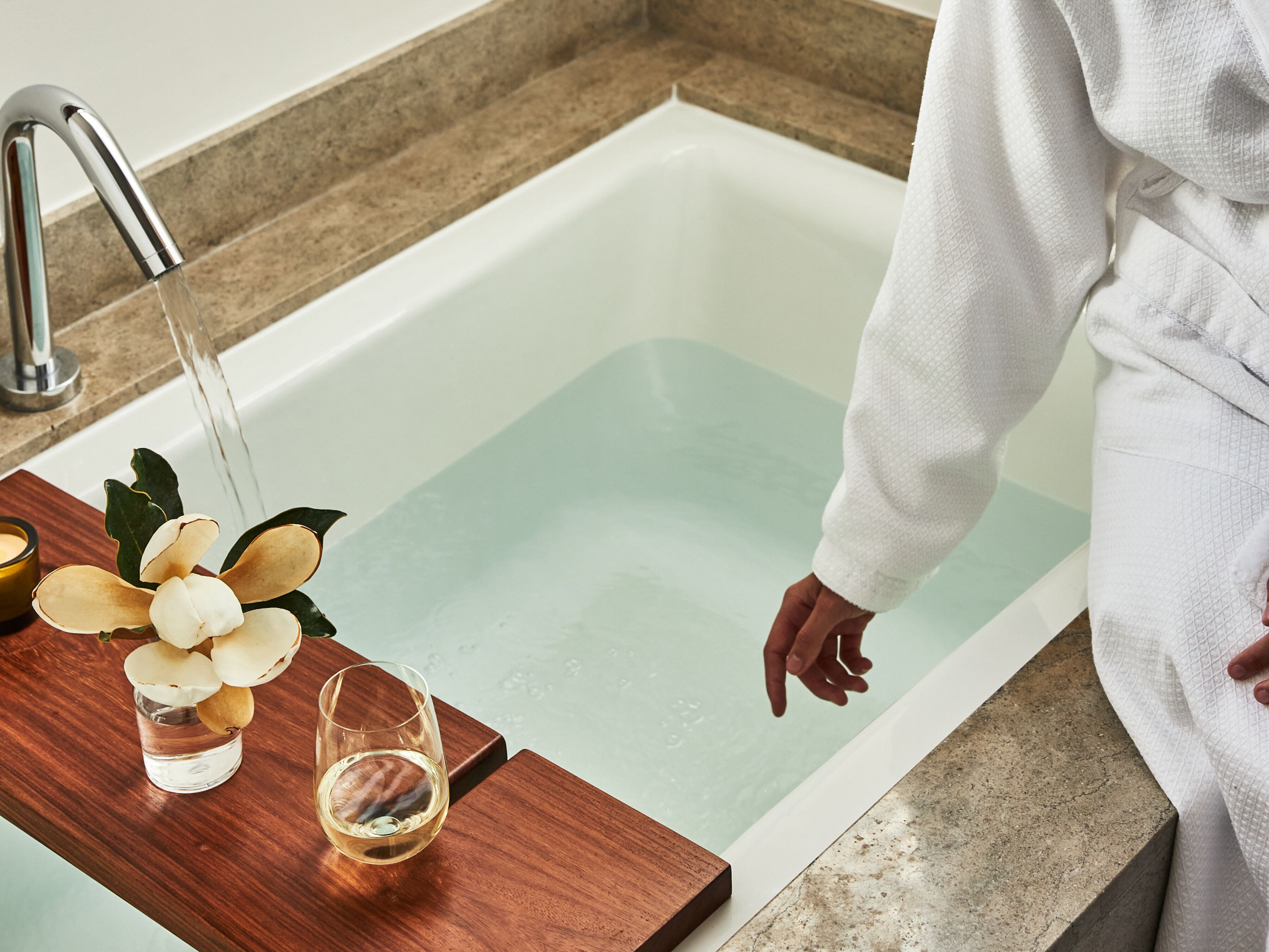 A bathtub with a wooden tray holding a glass of water and a flower arrangement.