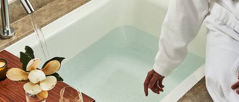 A bathtub with a wooden tray holding a glass of water and a flower arrangement.