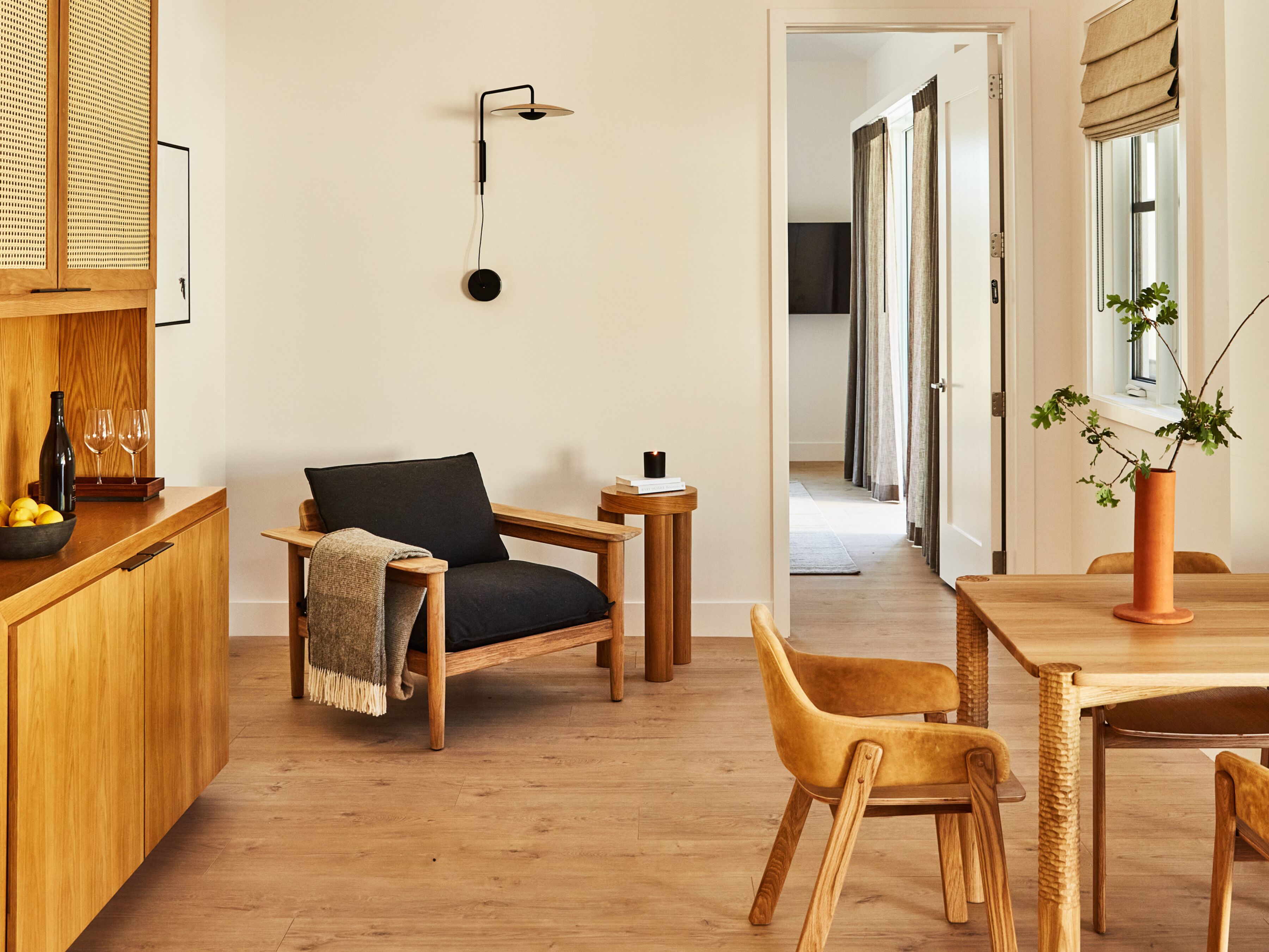 A modern kitchen with wooden cabinets, a black chair, a wooden dining table, and a hanging light fixture.