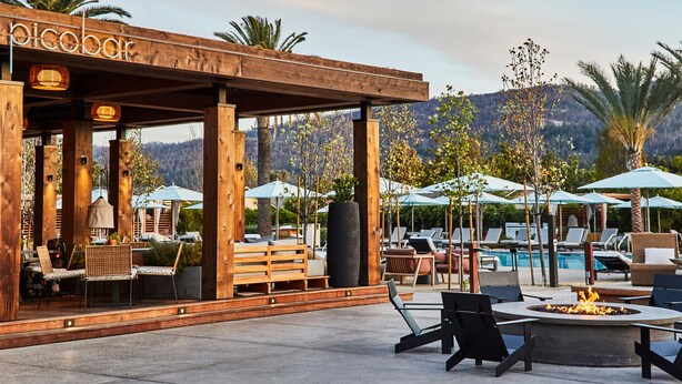 A wooden outdoor seating area with a fire pit, lounge chairs, and umbrellas. - Solage, Auberge Collection (Calistoga)