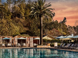 A pool area with lounge chairs and umbrellas, surrounded by trees and a palm tree.