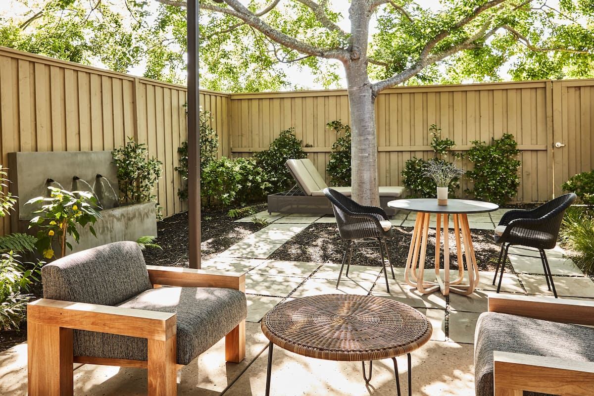 A patio with a wooden table and chairs, surrounded by a wooden fence and greenery.