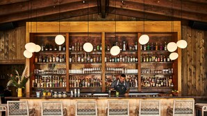 A bar with wooden shelves stocked with liquor bottles, a bartender at the counter, and wicker bar stools. - Solage, Auberge Collection (Calistoga)