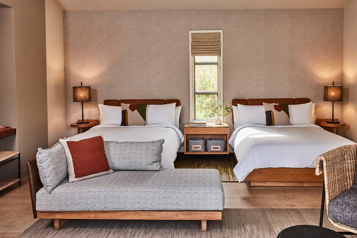 A hotel room with two beds, a sofa, and a chair.