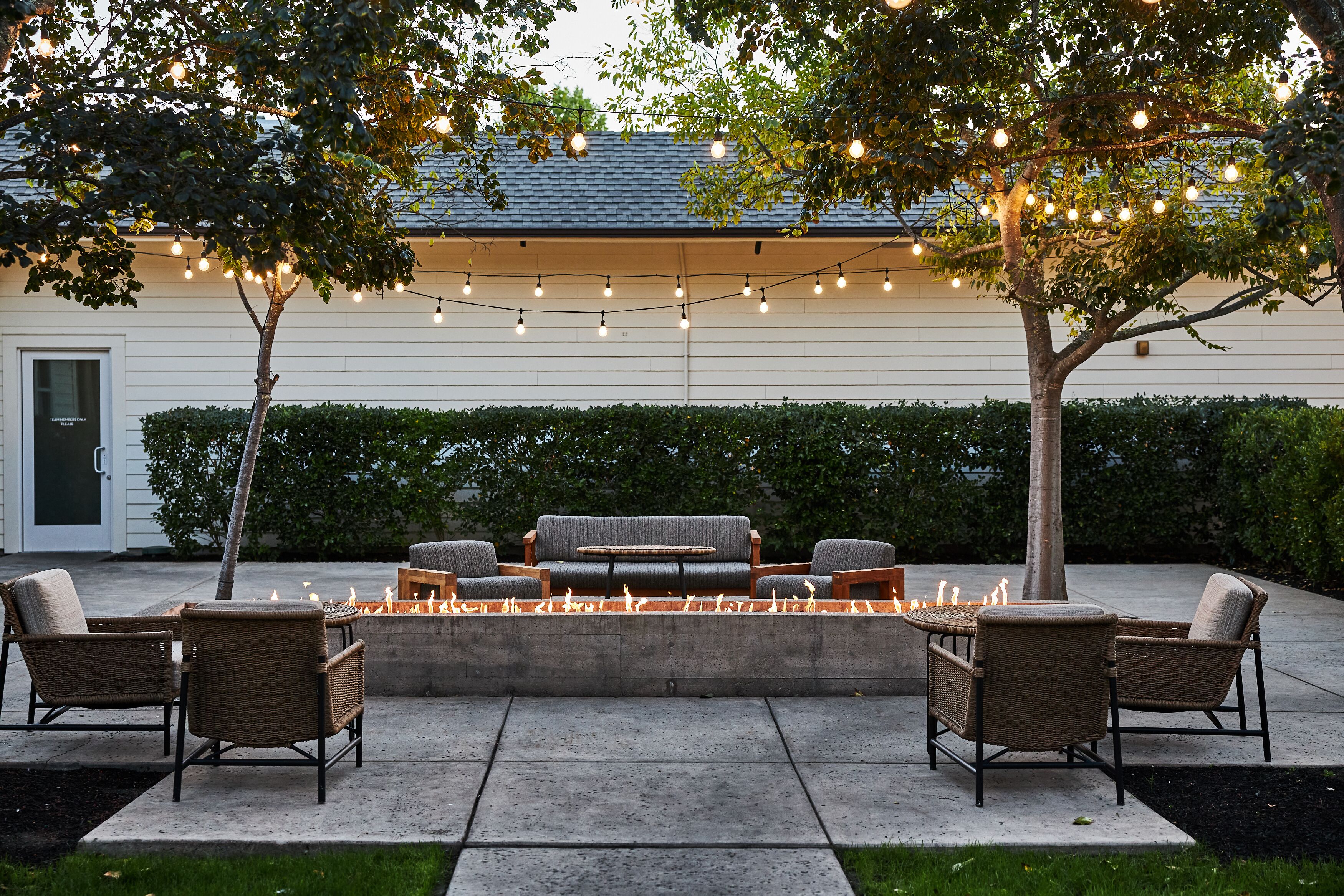 An outdoor seating area with wicker furniture, a fire feature, and string lights.