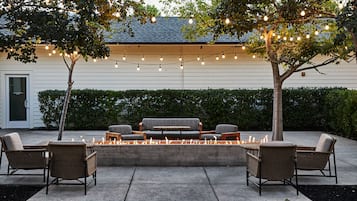 An outdoor seating area with wicker furniture, a fire feature, and string lights.
