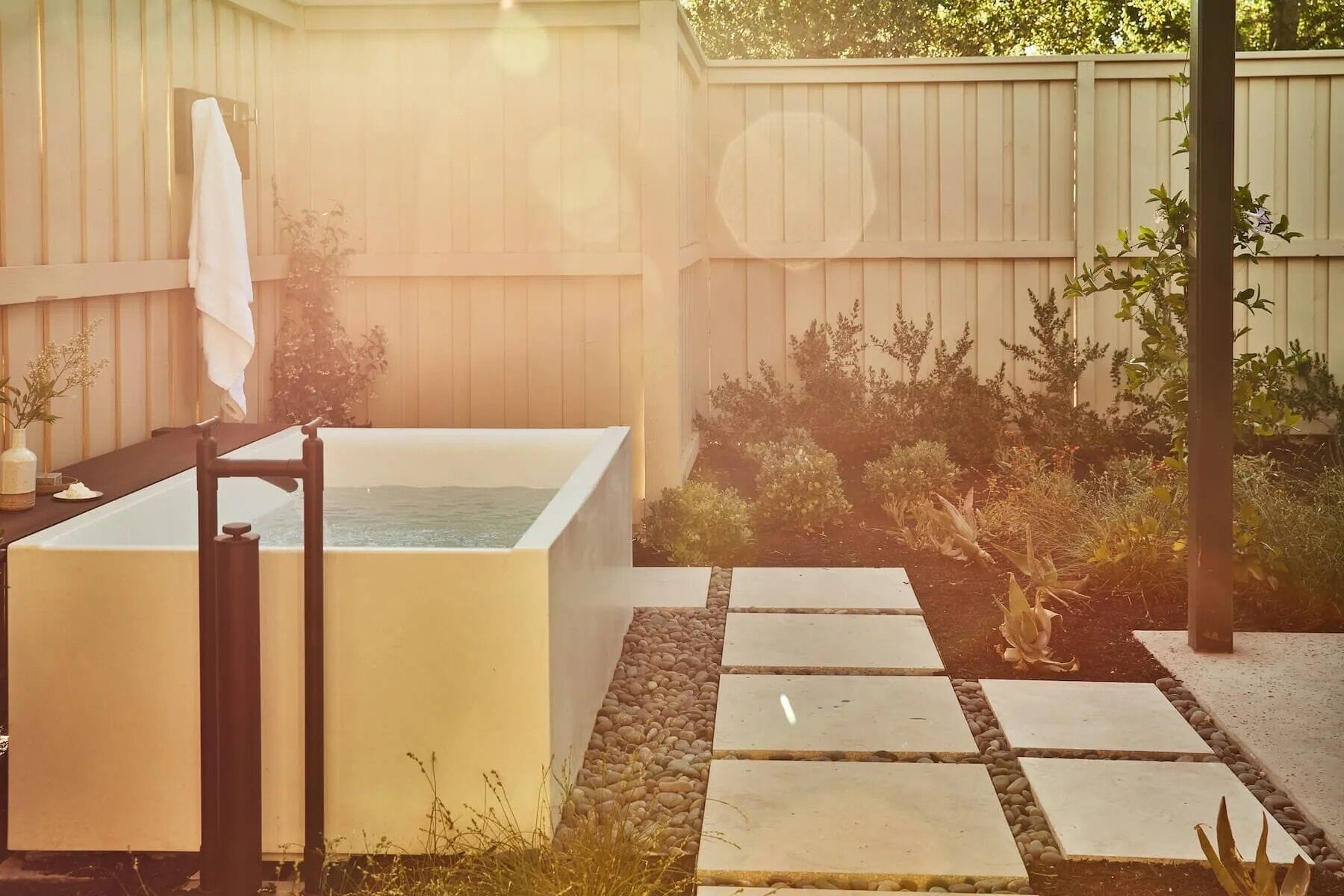 A spa area with a large bathtub, a towel rack, and a stone pathway.