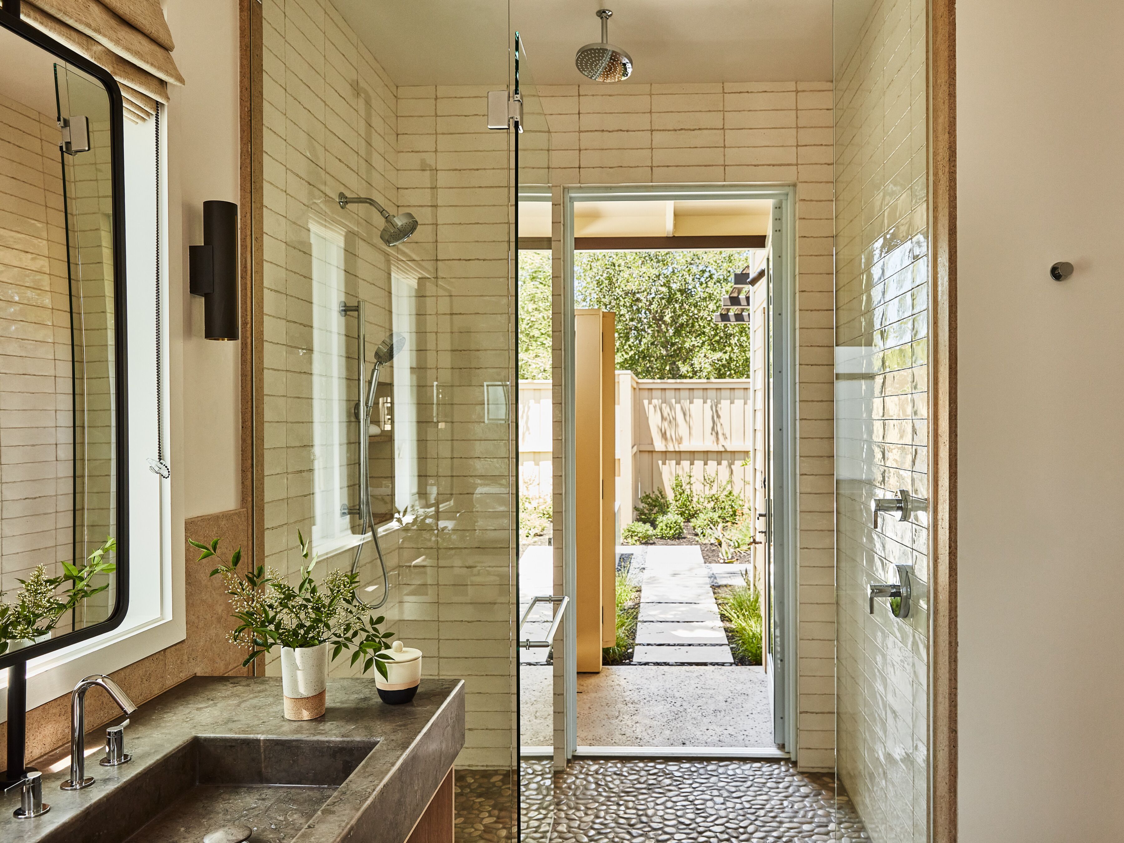 A modern bathroom with a glass shower enclosure, a double sink, and a potted plant on the counter.