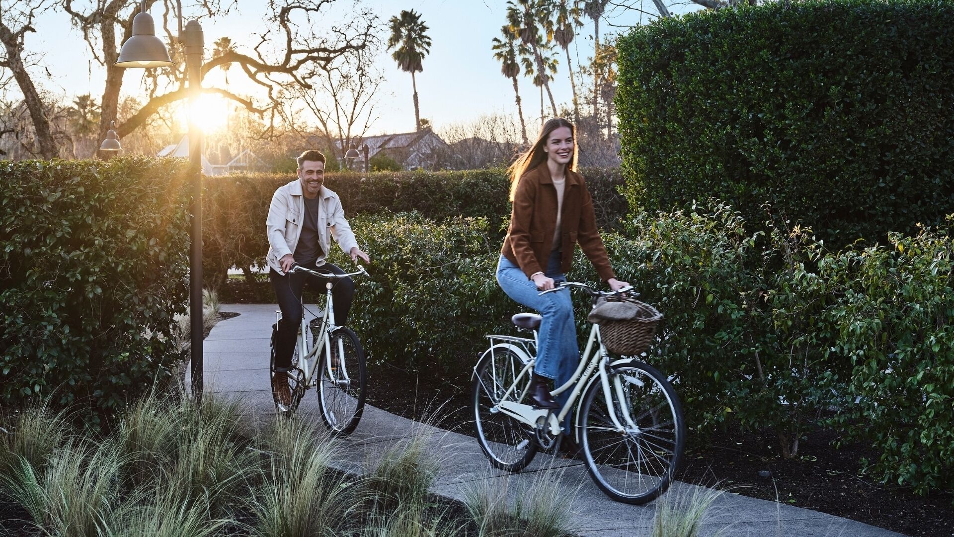 Two people riding bicycles on a paved path surrounded by greenery and trees.
